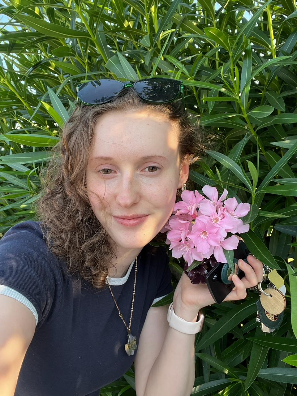 Sarah draußen zwischen grünen Pflanzen und rosafarbenen Blüten